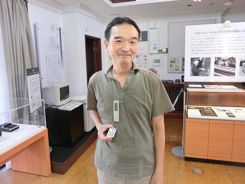 ペンダント電卓を首にかけた尾﨑 久高さんの画像